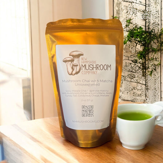 Pictured is a gold bag filled with mushroom chai with matcha tea sitting on a wood countertop next to a cup of matcha tea