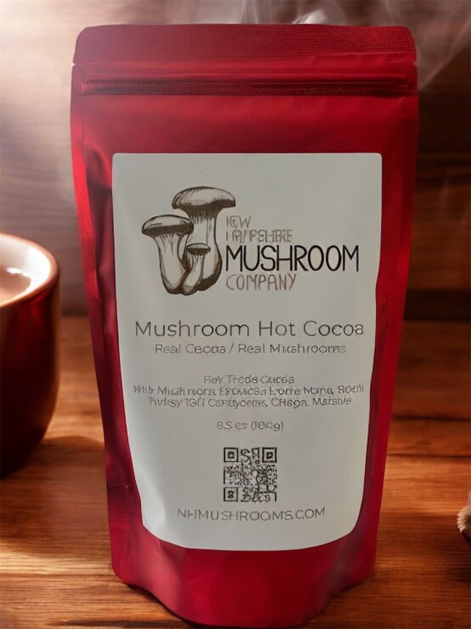 A picture of a red bag with mushroom hot cocoa inside sitting on a wood countertop next to a cup of hot cocoa